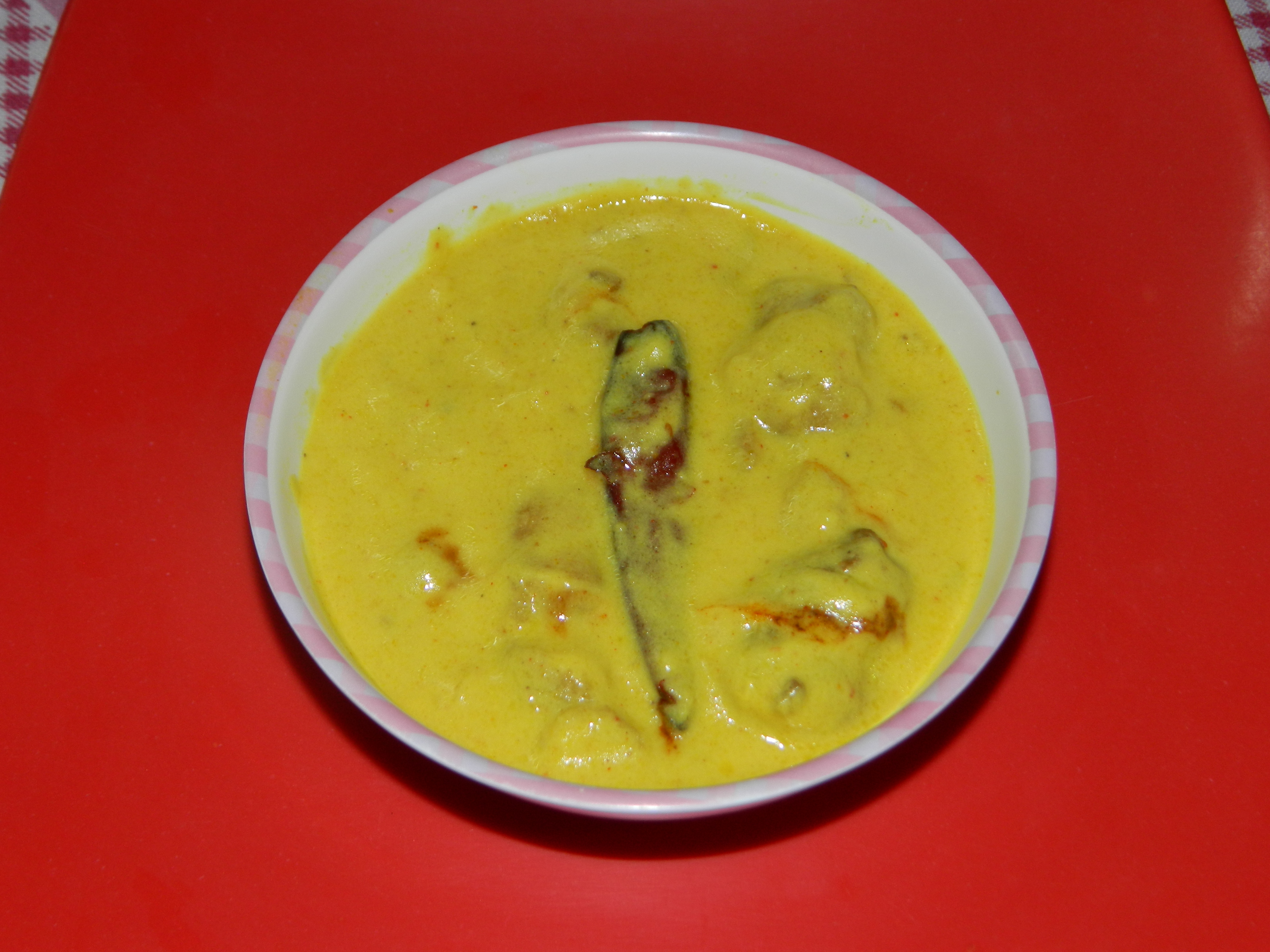 Warm yellow kadhi garnished with red chilli